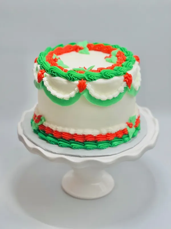 Round white buttercream cake with red and green piped shell borders, swags and holly leaves