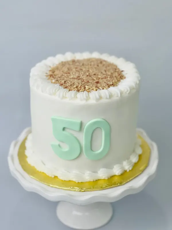 White buttercream cake topped with chopped nuts and a mint green fondant 50 on the side
