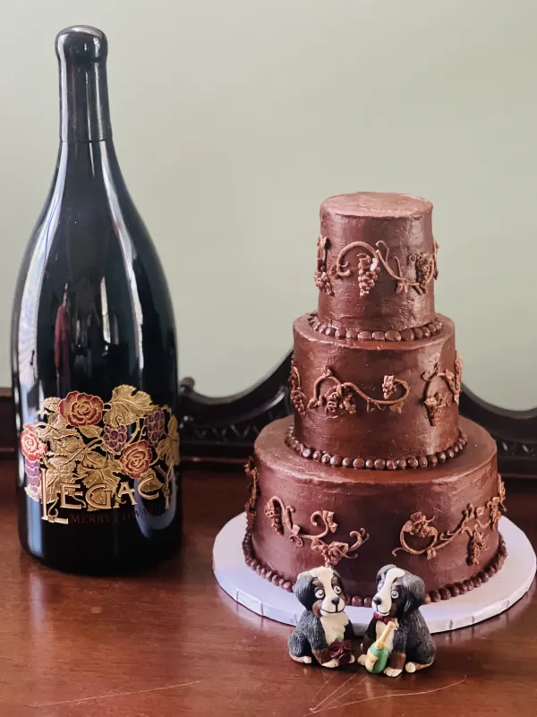 Three-tier chocolate cake with piped grapevines and two Bernese mountain dog figures