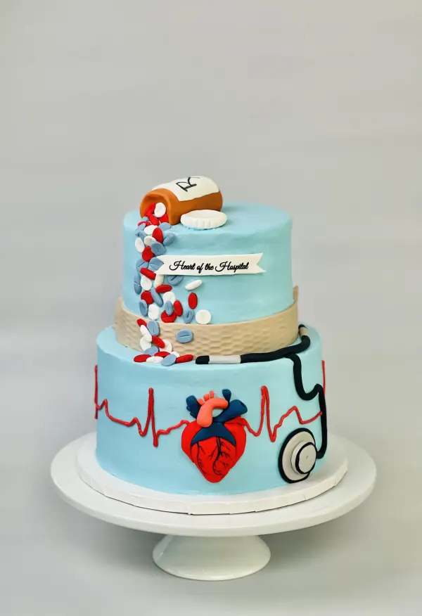 Two-tier blue cake with a pill bottle, anatomical heart, EKG line and Heart of the Hospital banner