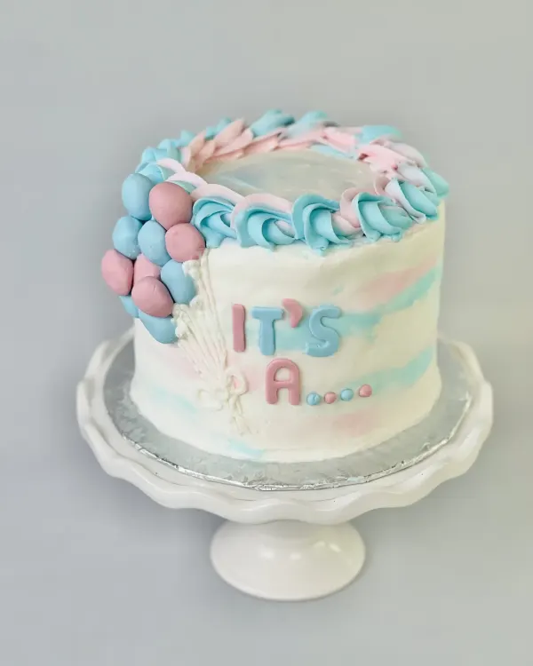 Pink and blue watercolor cake with a fondant balloon cluster and IT'S A ... lettering