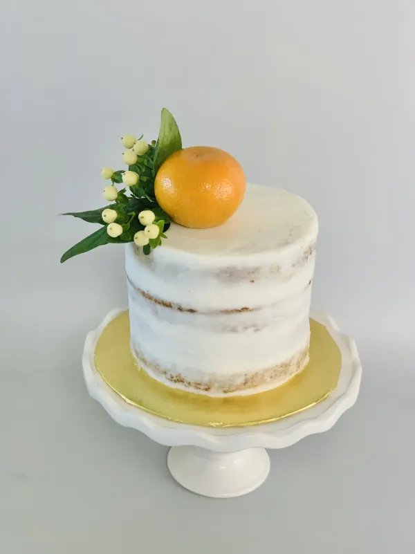 Semi-naked white buttercream cake topped with a whole mandarin, white berries and greenery