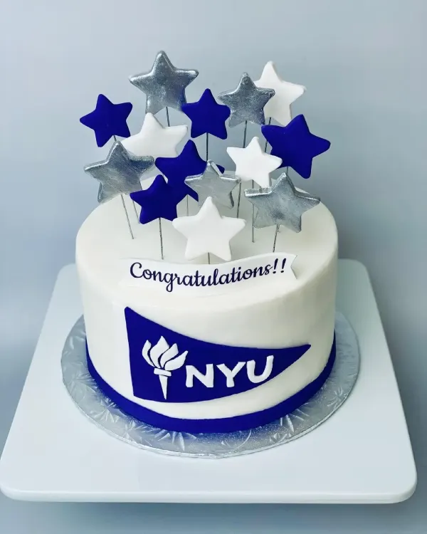 White fondant cake with a navy NYU pennant, Congratulations banner and star picks