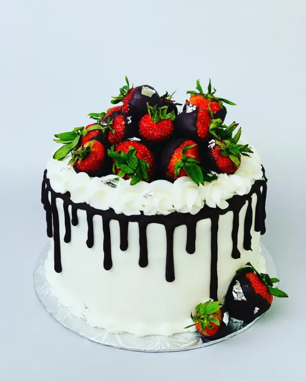 White buttercream cake with dark chocolate drip and chocolate-dipped strawberries with silver leaf