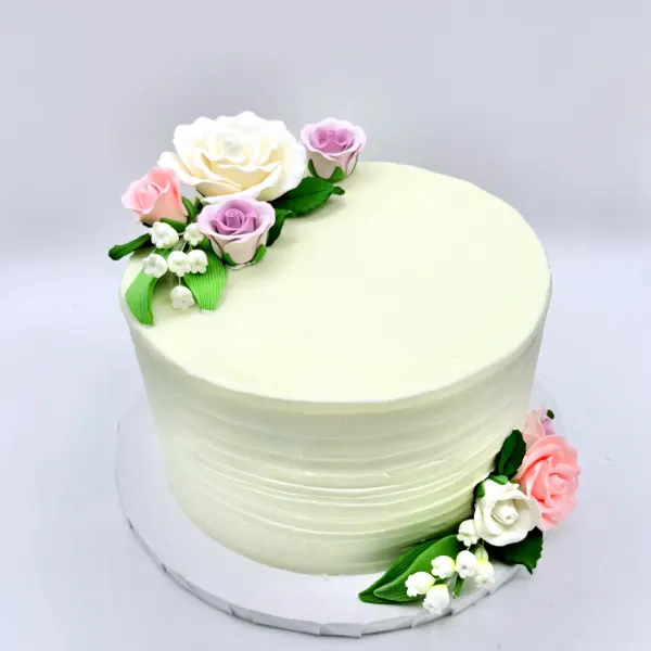 Ivory textured buttercream cake with sugar roses in white, pink and lavender and small green leaves