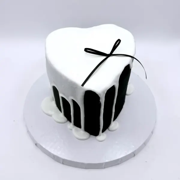 White heart shaped cake with a black drip down the sides and a thin black bow on top