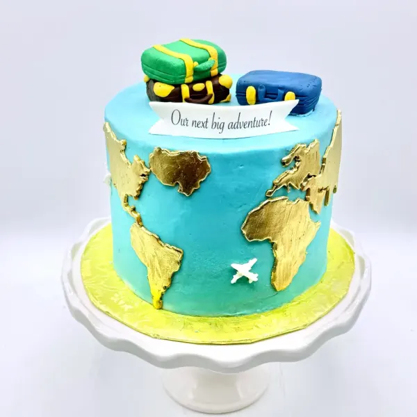 Turquoise cake with gold world map continents, a small plane and fondant suitcases on top
