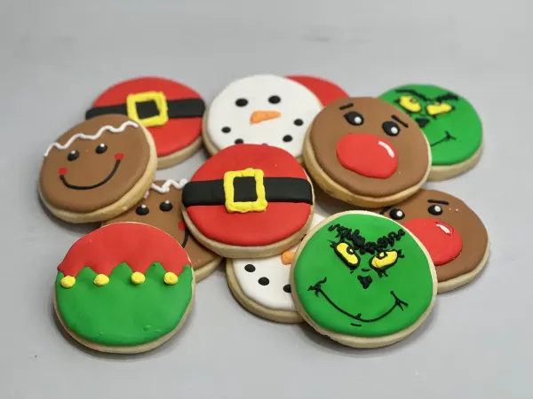 Round Christmas cookies iced as gingerbread, snowman, reindeer, elf, Santa belt and Grinch faces