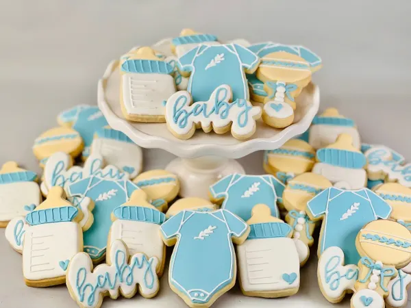 Blue and white baby shower cookies shaped as onesies, bottles and rattles with baby in script