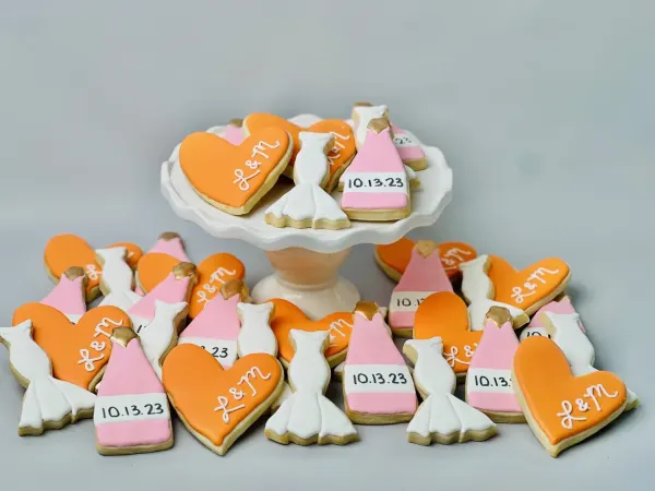 Orange heart cookies iced L and M with pink champagne bottles dated 10.13.23 and white gowns