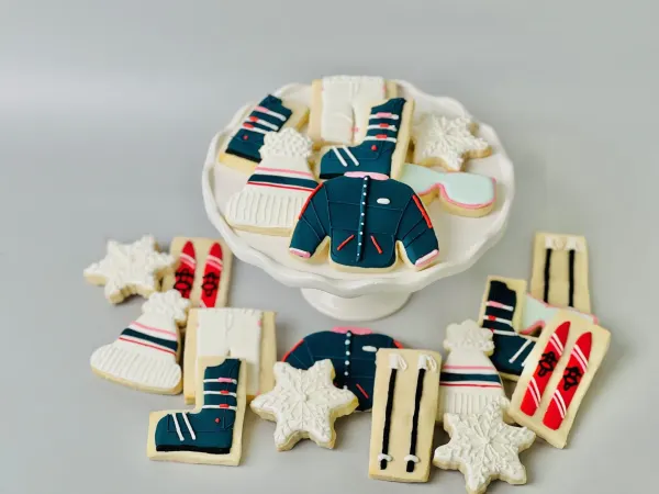 Ski themed cookies with navy puffer jacket, boots, beanie, goggles, red skis and snowflakes