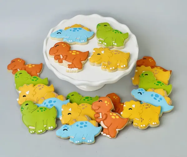 Dinosaur cookies iced in green, orange, blue and yellow on a white cake stand