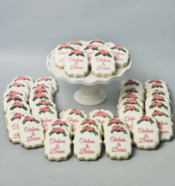 White plaque cookies with pink piped roses lettered Chelsea and Brian in script