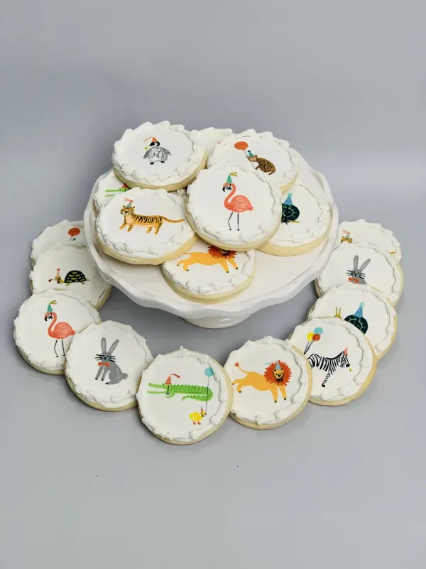 Round white-iced cookies with printed party animals in party hats including flamingo, tiger and zebra