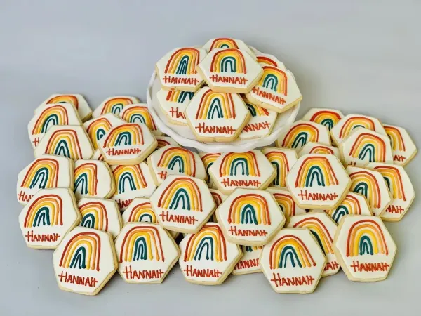 Hexagon cookies iced in cream with retro rainbow arches and the name Hannah in orange