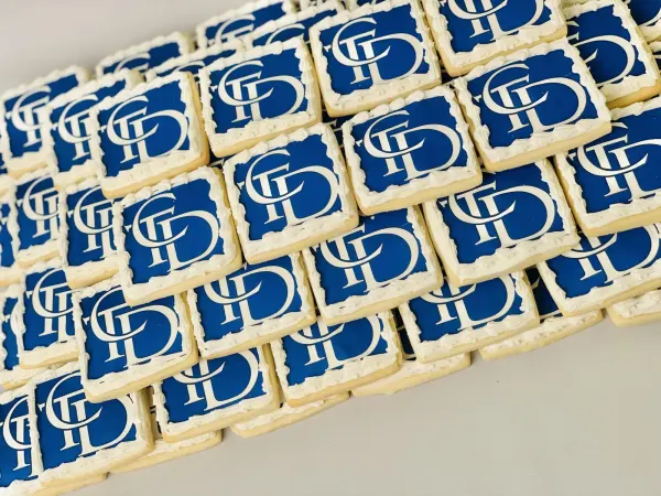 Rows of square cookies iced in royal blue with a white interlocking monogram logo