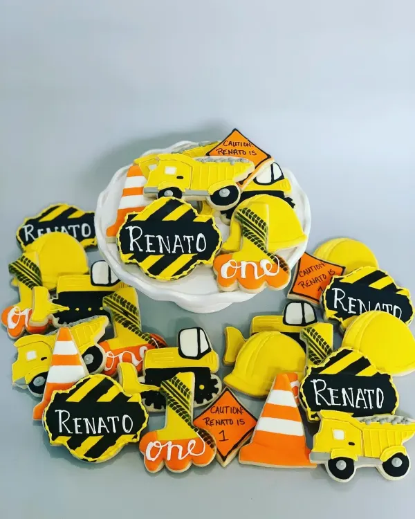 Construction cookie set with dump trucks, hard hats, cones and caution signs reading Renato is 1