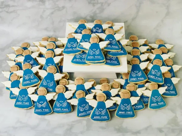 Dozens of angel-shaped sugar cookies in blue royal icing lettered ANGEL FUND with white wings