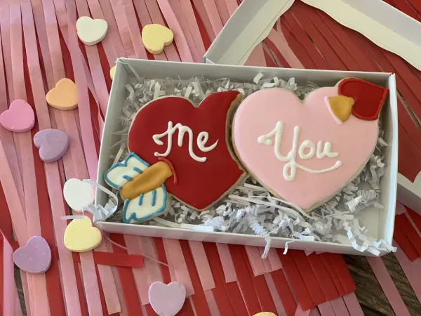 Boxed cookie set with a red heart piped Me, a pink heart piped You and a cupid arrow