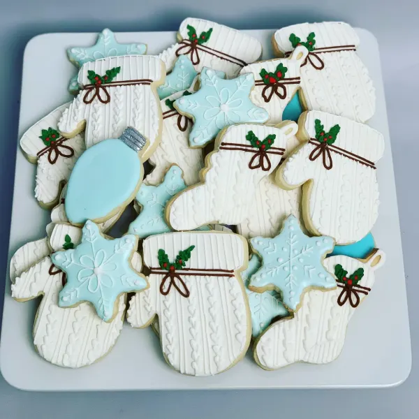 Platter of white cable-knit mitten cookies with holly bows plus aqua snowflake and ornament cookies