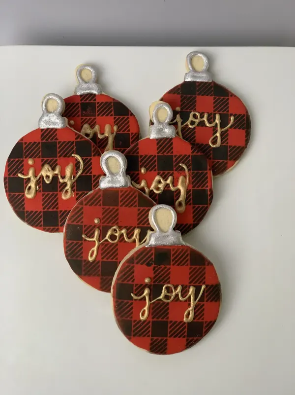 Round ornament cookies in red and black buffalo plaid lettered joy in gold with silver caps