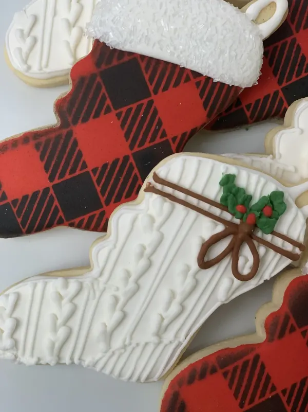 Close-up of buffalo plaid and white cable-knit stocking cookies with brown bows and holly