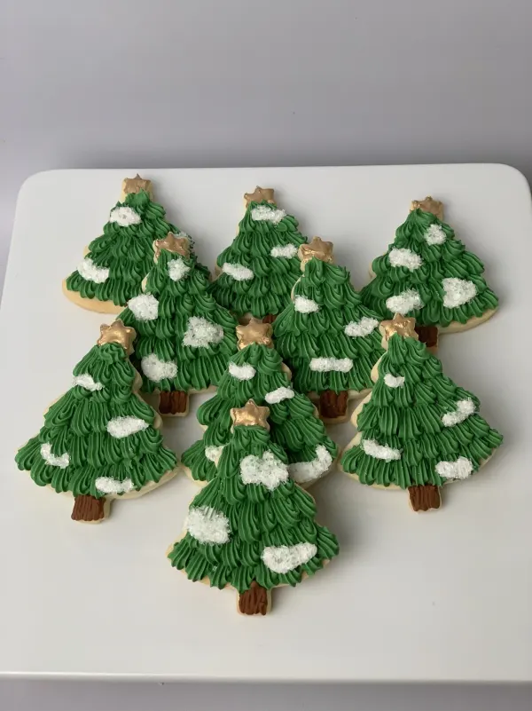 Christmas tree cookies piped in green buttercream with gold fondant stars and white snow