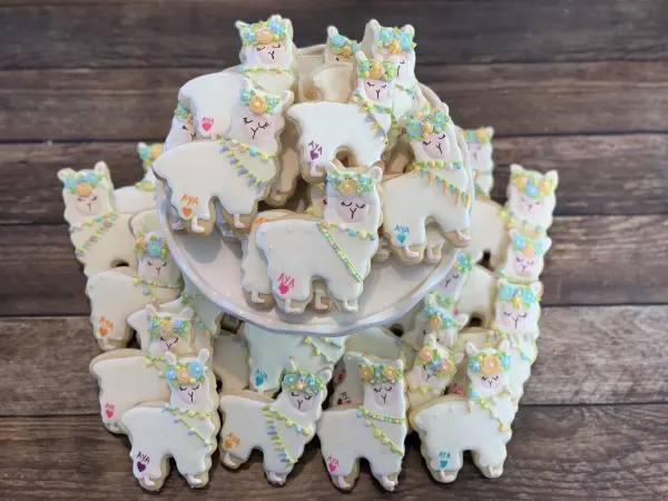 White llama cookies with pastel flower crowns, each lettered AYA with a small heart