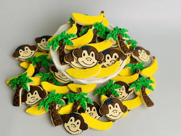 Monkey face cookies with blue bows alongside yellow banana and green palm tree cookies