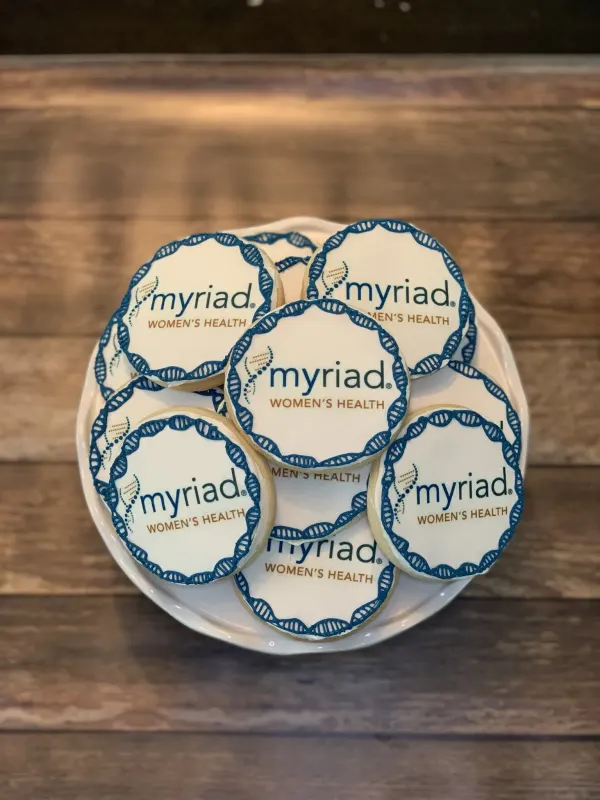 Round logo cookies printed Myriad Women's Health with a piped blue DNA helix border