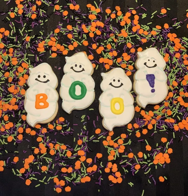 Four ghost cookies spelling BOO on a bed of Halloween sprinkles