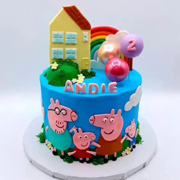 Blue cake with a fondant house, rainbow, balloons and pig characters, lettered Andie with a number two