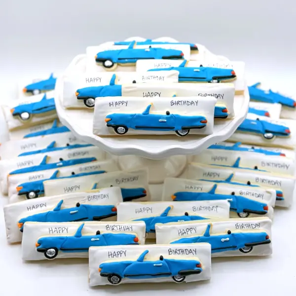 Blue convertible car cookies alongside plaque cookies lettered Happy Birthday