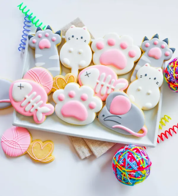 Cat cookies with faces, paw prints, fish bones and yarn balls in pink, grey and white