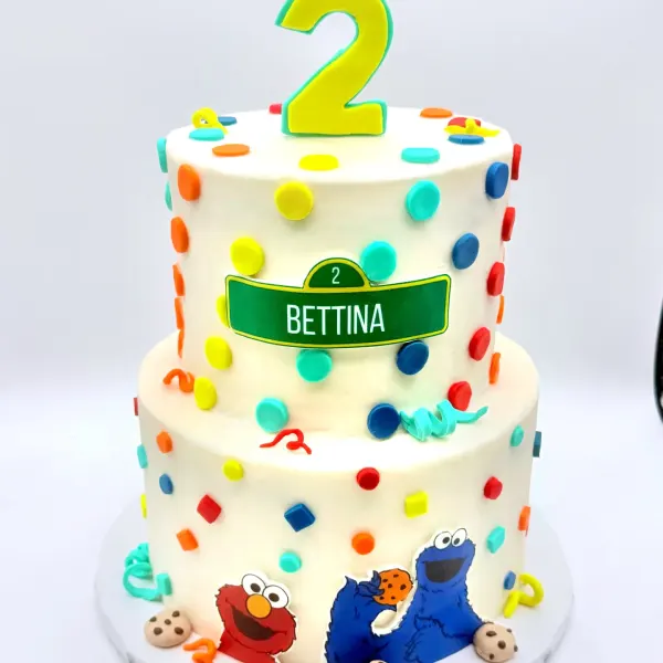 Two tier confetti dot cake with a Bettina plaque, a number two topper and character figures at the base