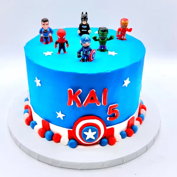 Blue cake with white stars, superhero figures on top and Kai and the number five in red