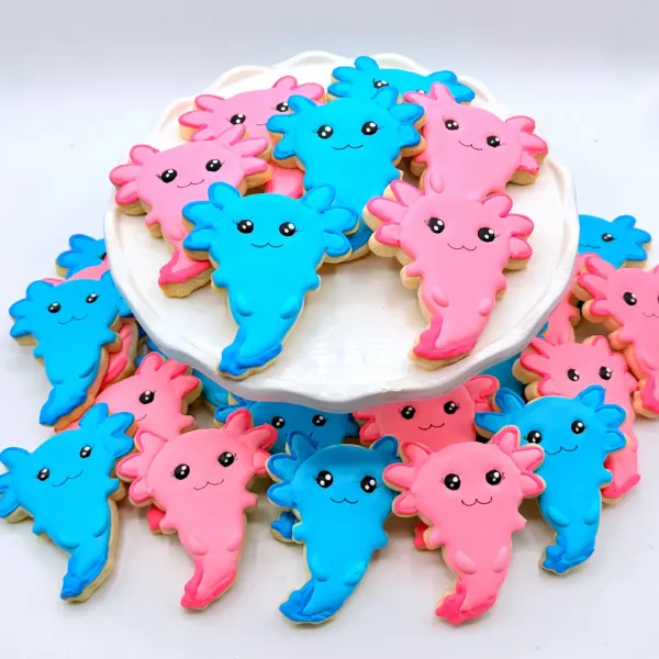Axolotl cookies in pink and blue with small smiling faces, piled on a white stand