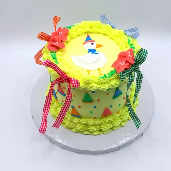 Yellow buttercream cake with a goose plaque, gingham ribbons and party hat confetti