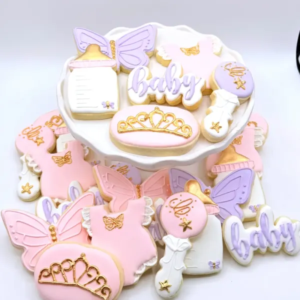 Pink and lavender baby shower cookies with butterfly wings, gold tiaras, onesies and rattles