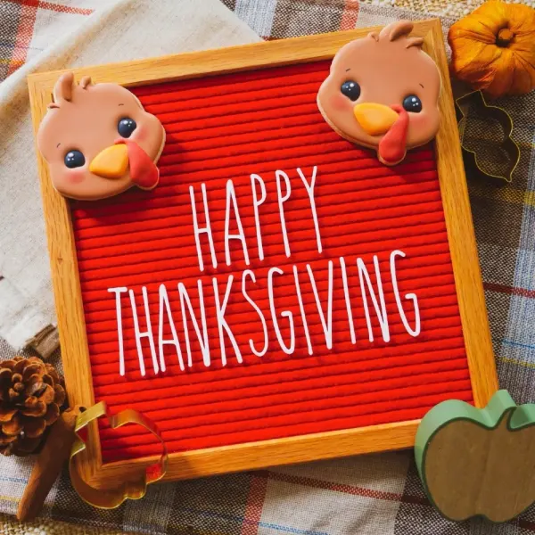 Turkey cookies at the corners of a red letterboard reading Happy Thanksgiving, with a pumpkin cookie