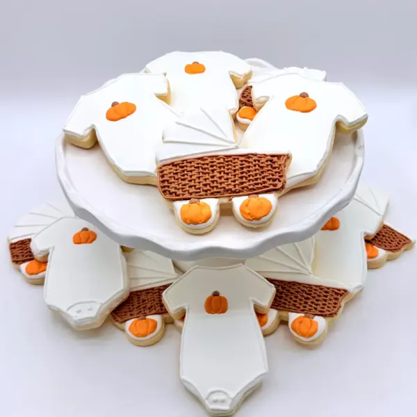 Fall baby shower cookies with white onesies, small orange pumpkins and a woven pram