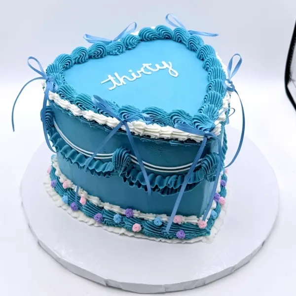 Blue heart shaped cake with ruffled piping, satin bows and thirty piped in white script on top