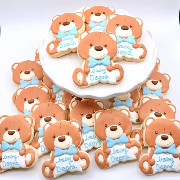 Teddy bear cookies in tan with blue bow ties, each lettered Baby Deora