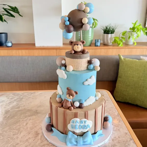 Two tier teddy bear cake with a blue cloud tier, a striped tier, a bear topper and a Baby Deora plaque