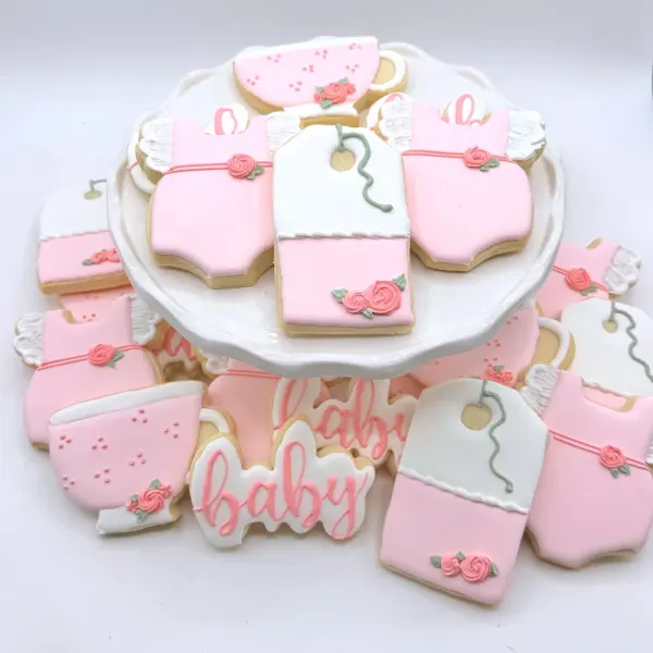 Pink and white baby cookies with rose trimmed onesies, bottles and baby lettered in pink script