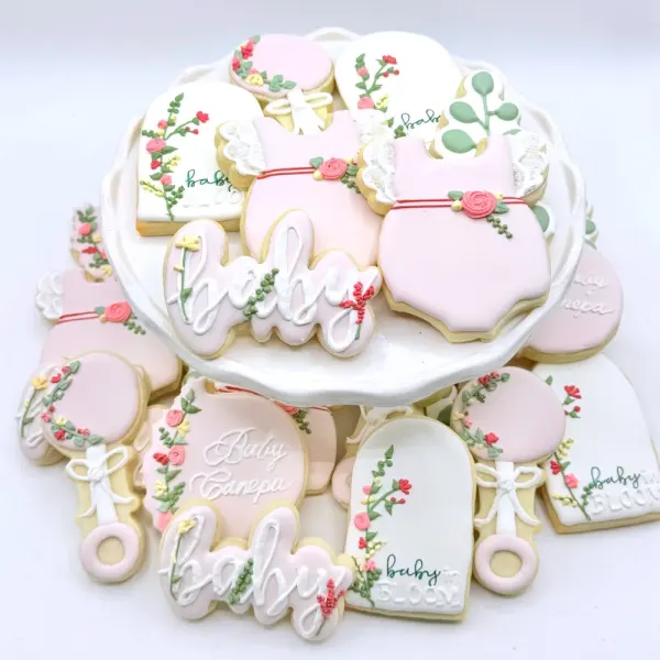 Pink baby shower cookies with floral vines, onesies, rattles and baby lettered in white script