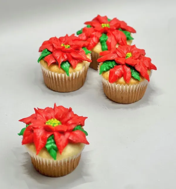 Four cupcakes topped with piped red buttercream poinsettias and green leaves