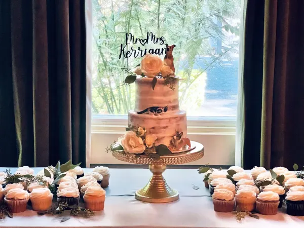 Two-tier blush semi-naked cake with dog figures and a Mr and Mrs Kerrigan topper above pink cupcakes
