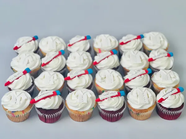 Cupcakes with white buttercream swirls topped with fondant lab coats and red syringes