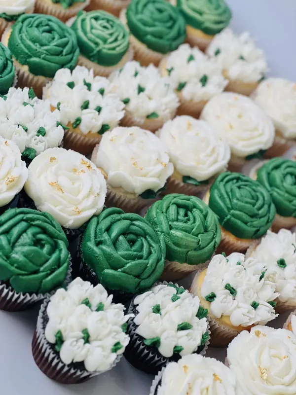 Cupcakes piped with green and white buttercream roses and flower clusters with gold leaf flecks